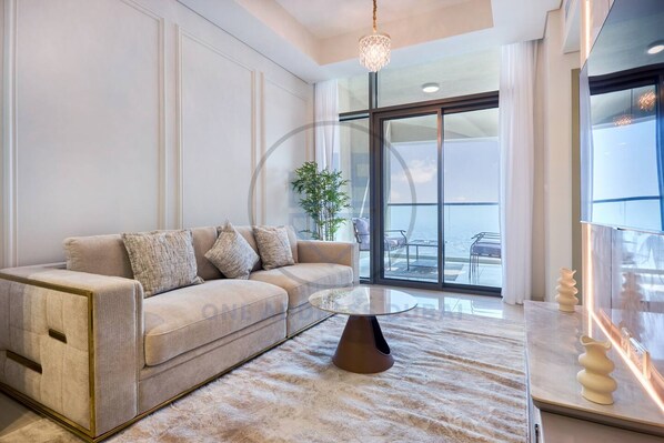 A modern living room with a sofa, a coffee table, and a large window offering a view of the outdoors. - Sky-high 2BR in Aykon City Panoramic Views (Dubai)