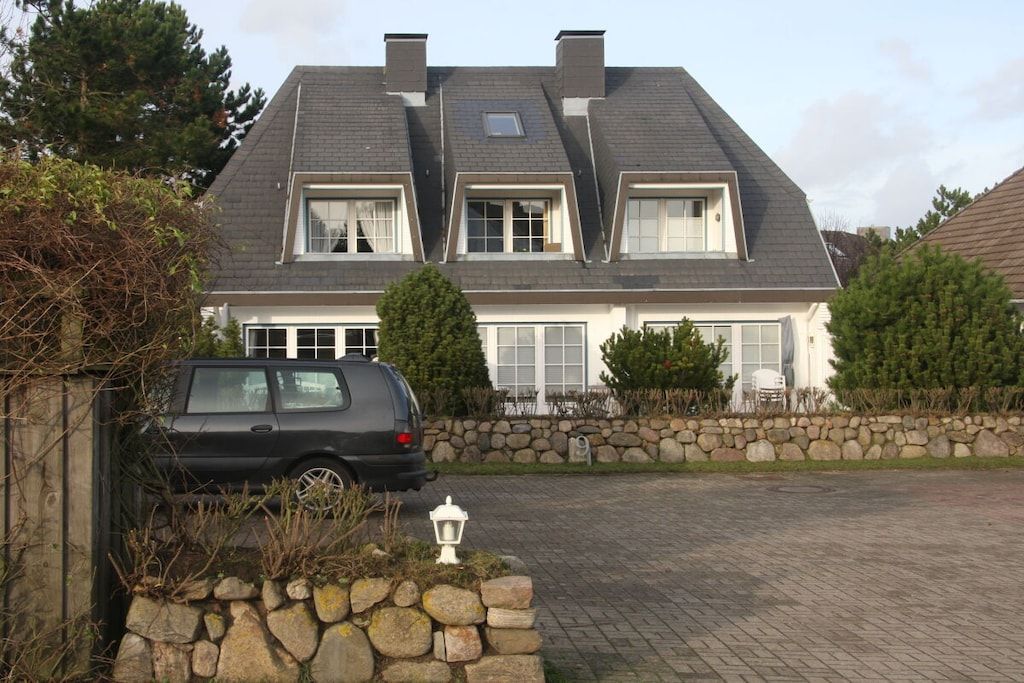A two-story house with a stone wall and a paved driveway.