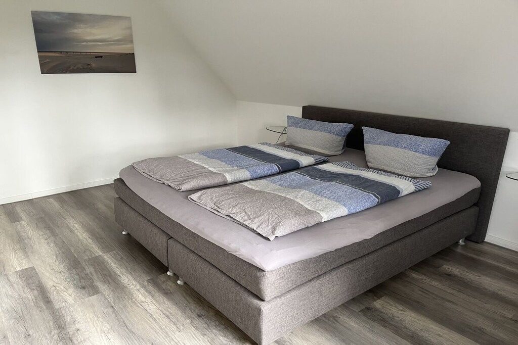 A single bed with a grey headboard and a grey mattress, a grey blanket, and two pillows with a blue and white pattern.
