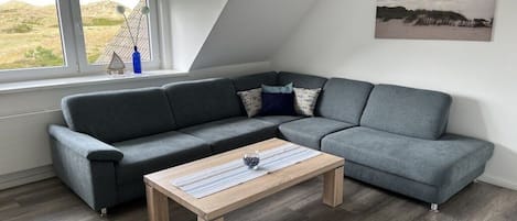 A modern living room with a grey sectional sofa, a wooden coffee table, and a view of the outdoors through a window.