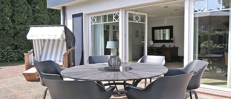An outdoor patio with a round table and chairs, a grill, and a covered seating area.