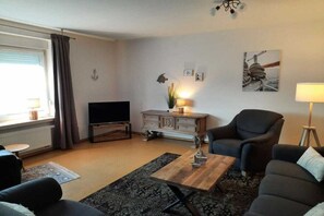 A living room with a sofa, armchair, coffee table, TV, and decorative items. - Holiday apartment in Varel with swimming pool (Varel)