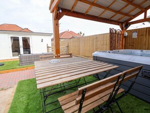 Eine Außenpatio mit einem Holztisch und Bänken, einem Whirlpool und einem überdachten Sitzbereich.