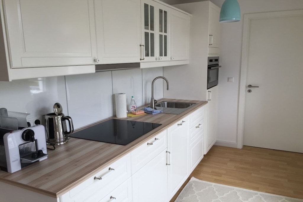 A kitchen with white cabinets, a black induction cooktop, a stainless steel kettle, and a blue pendant light.