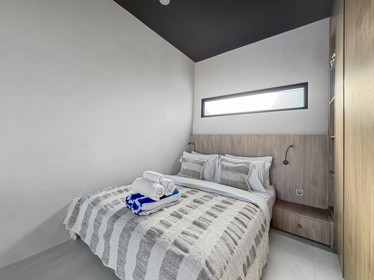 A modern bedroom with a bed, a bedside table, a wall-mounted light, and a wooden wardrobe.