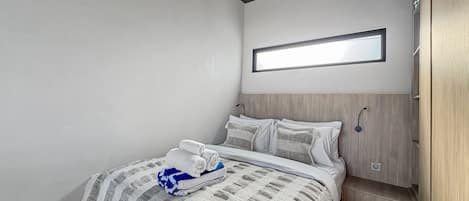 A modern bedroom with a bed, a bedside table, a wall-mounted light, and a wooden wardrobe.