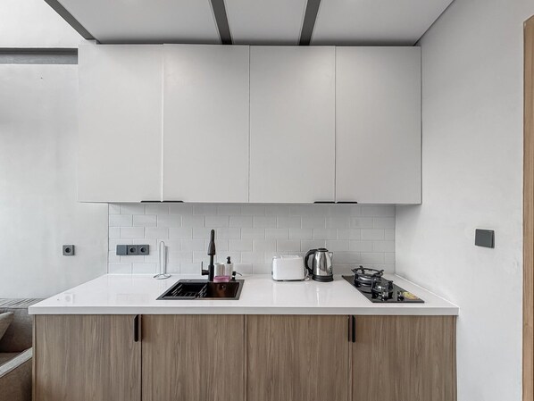 A modern kitchen with a white countertop, wooden cabinets, a kettle, a toaster, and a stove. - Canggu Private Pool Villa (Canggu)