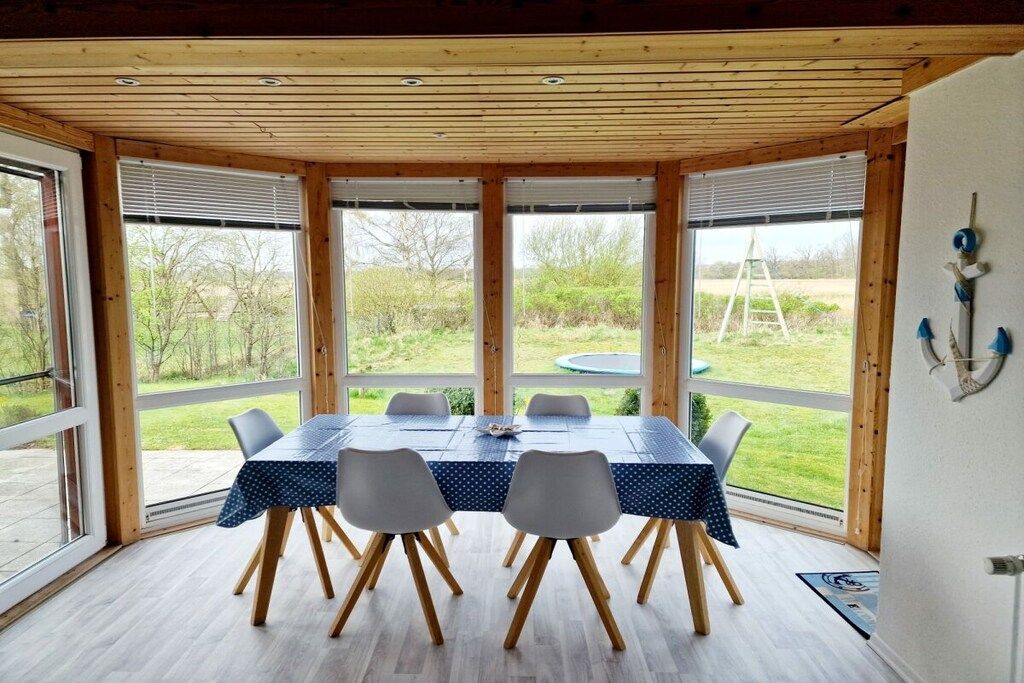 Een eethoek met een tafel, stoelen, grote ramen en uitzicht op de omgeving.