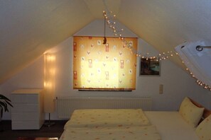 A bedroom with a sloped ceiling, a bed with floral bedding, a radiator, and string lights. - Holiday home in Daschow with swimming pool (Daschow)