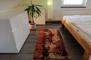 Une chambre à coucher avec un lit, une commode, un radiateur, une fenêtre et une plante.