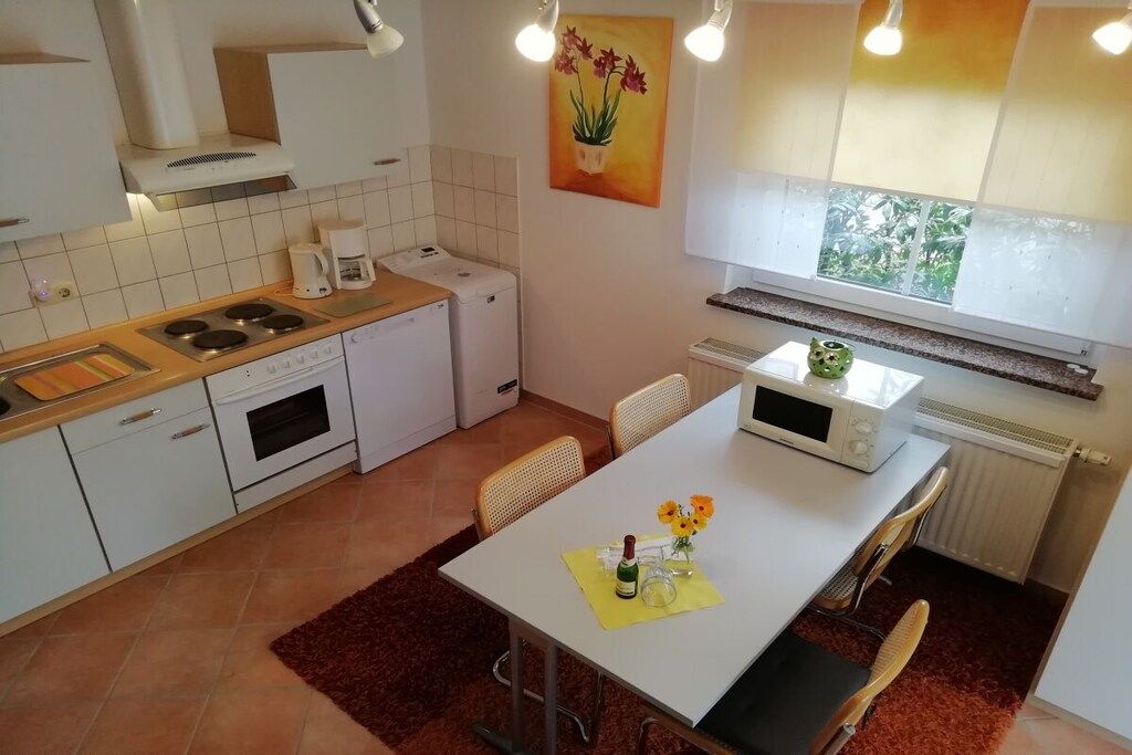 A compact kitchen with white cabinets, a stove, a microwave, and a dining area with a table and chairs.