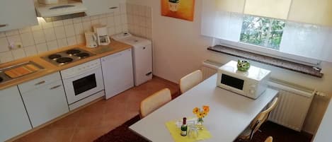 Une cuisine compacte avec des meubles blancs, une cuisinière, un four à micro-ondes et un coin repas comprenant une table et des chaises.
