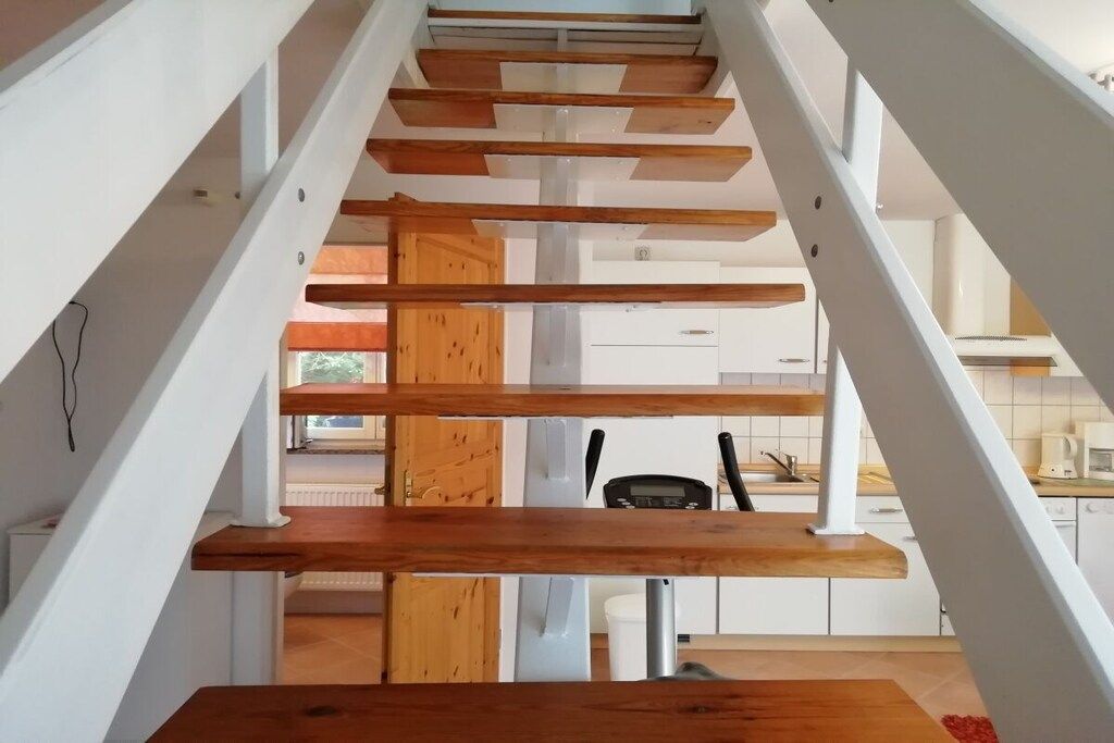 A modern staircase with wooden steps and white railings leading to an upper floor.