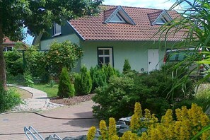 A house with a sloped roof, a paved driveway, and a garden with various plants and flowers. - Holiday home in Daschow with swimming pool (Daschow)