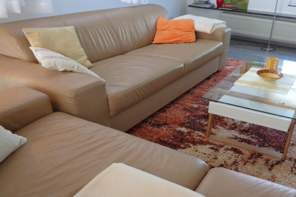 A beige sofa with cushions, a glass coffee table, and a patterned rug.
