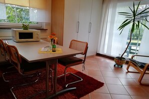 Un espace repas comprenant une table, des chaises, un four à micro-ondes, une plante en pot et une fenêtre donnant sur un paysage verdoyant.