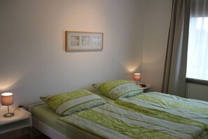 A single bed with a green and white striped bedspread, two bedside lamps, a framed picture on the wall, and a window with curtains. - Holiday apartment in Büsum with swimming pool (Büsum)