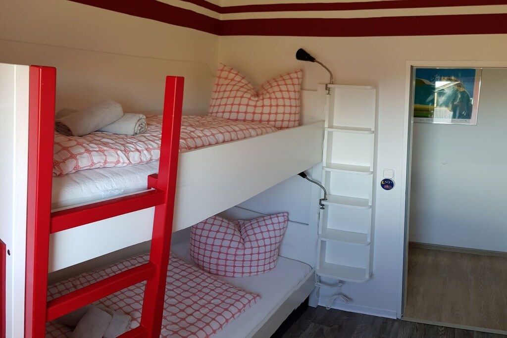 Une chambre avec un lit superposé, une échelle, une armoire blanche et une porte ornée d’une affiche.