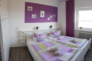 A room with two beds, a purple accent wall, and a window with a view. - Hesse "Bi"d Achterdör" (Langeoog)