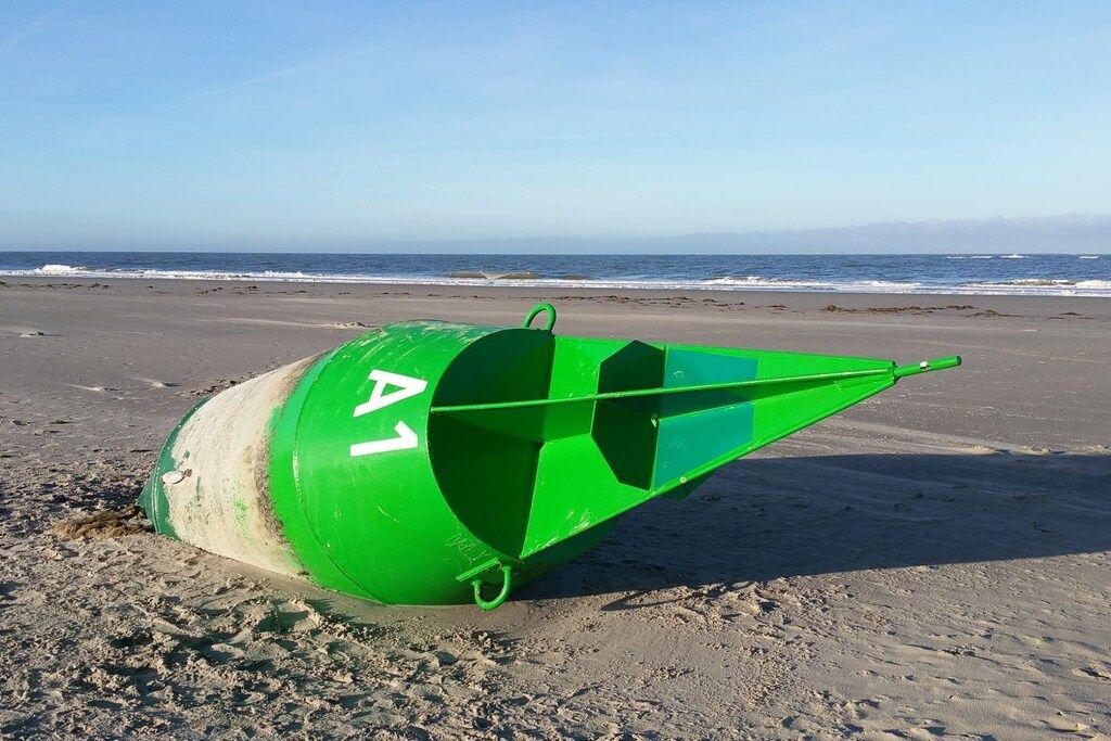 A green lifebuoy on a sandy beach with the ocean in the background.