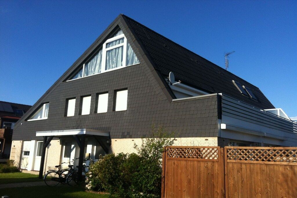 Een huis met twee verdiepingen, een schuin dak, een garage en een houten omheining.
