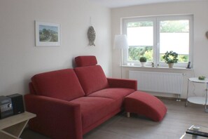 A red sofa in a room with a window, radiator, and a small table with a plant. - Dat Fischerhus - Ground Floor (Büsum)
