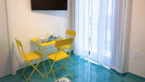 Une pièce dotée d’un téléviseur à écran plat fixé au mur, d’une table à manger avec des chaises jaunes et d’une fenêtre ornée de rideaux légers.