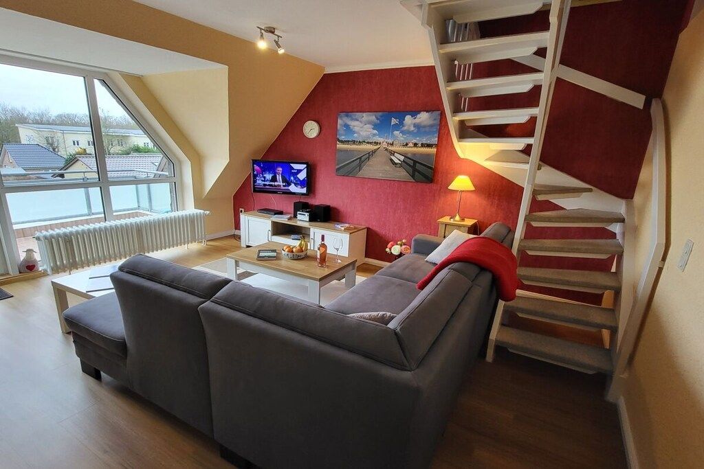 Een woonkamer met een bank, een salontafel, een televisie, een schilderij, een lamp en een trap.