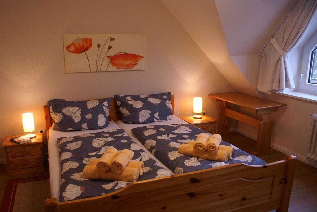 Un dormitorio con cama, dos mesitas de noche, un armario auxiliar, una ventana con cortinas y un cuadro en la pared.