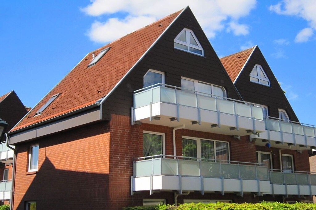 Un immeuble résidentiel de deux étages avec une façade en briques, un balcon doté de rampes en verre et un toit recouvert de tuiles rouges.