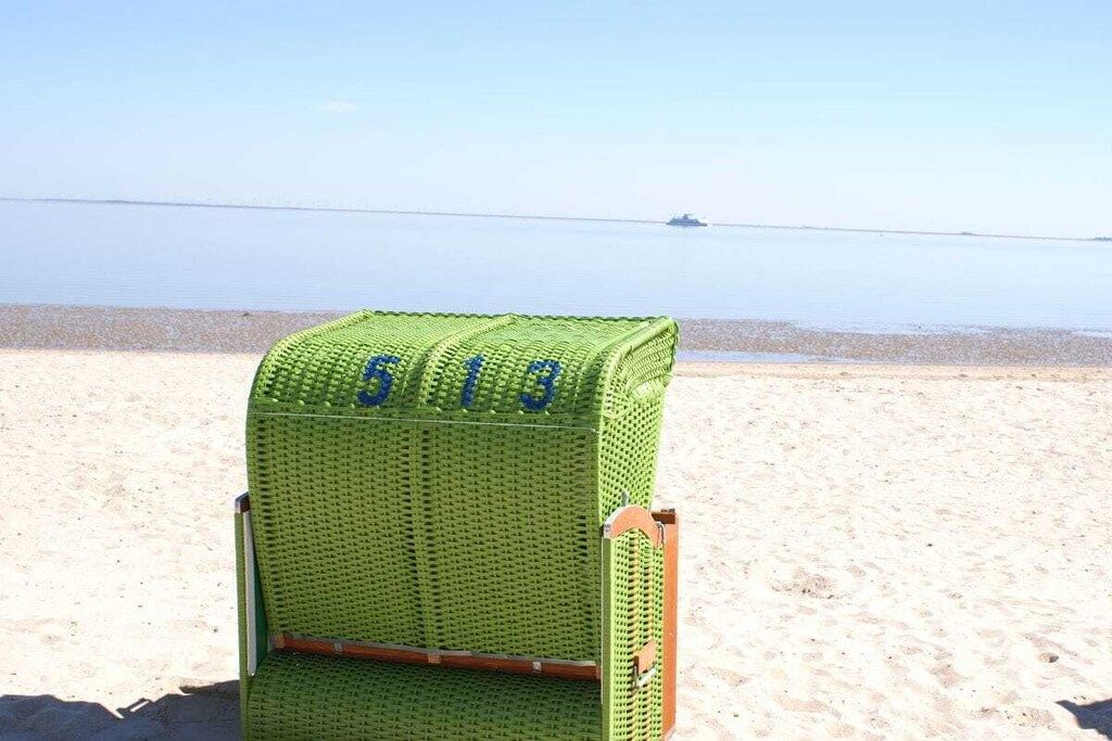 A green beach chair with the number 619 on it, placed on a sandy beach with a calm sea in the background.