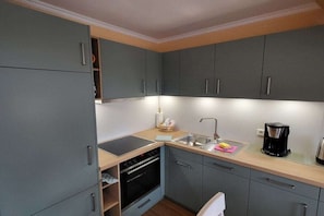 A compact kitchen with grey cabinets, a built-in oven, a sink, and a coffee maker. - in the Seeadler building at number 9 (Wyk)