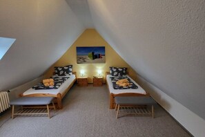 A small, triangular attic bedroom with two single beds, each with a pillow and a small bedside table with a lamp. - in the Seeadler building at number 9 (Wyk)