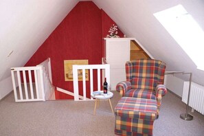 A small room with a red wall, a plaid chair, a small table with a bottle, and a radiator. - in the Seeadler building at number 9 (Wyk)