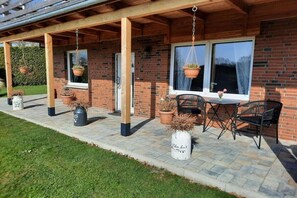 Un patio couvert agrémenté de jardinières suspendues et de meubles d’extérieur.