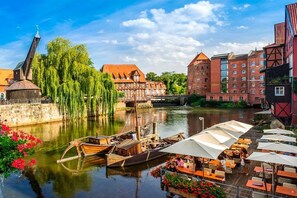 A riverside view with a traditional building, a wooden boat docked, and outdoor seating by the water. - Holiday apartment in Wesel with swimming pool (Wesel)