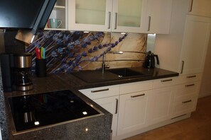 A kitchen with a black induction cooktop, white cabinets, a backsplash with a floral pattern, and a coffee maker. - Holiday apartment with 2 bedrooms (Wangerooge)