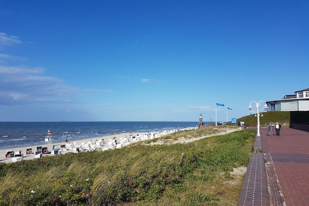 En kystpromenade med strandstole og parasoller, et fyrtårn og en klar blå himmel.