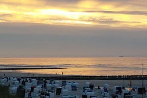 Ein Strand mit Reihen von Liegestühlen und Sonnenschirmen, ein hölzerner Steg und das Meer.