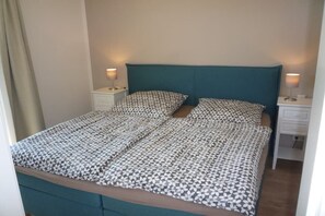Ein Einzelbett mit einem gemusterten Überwurf, zwei Nachttische mit Lampen und ein türkisblaues Kopfteil.