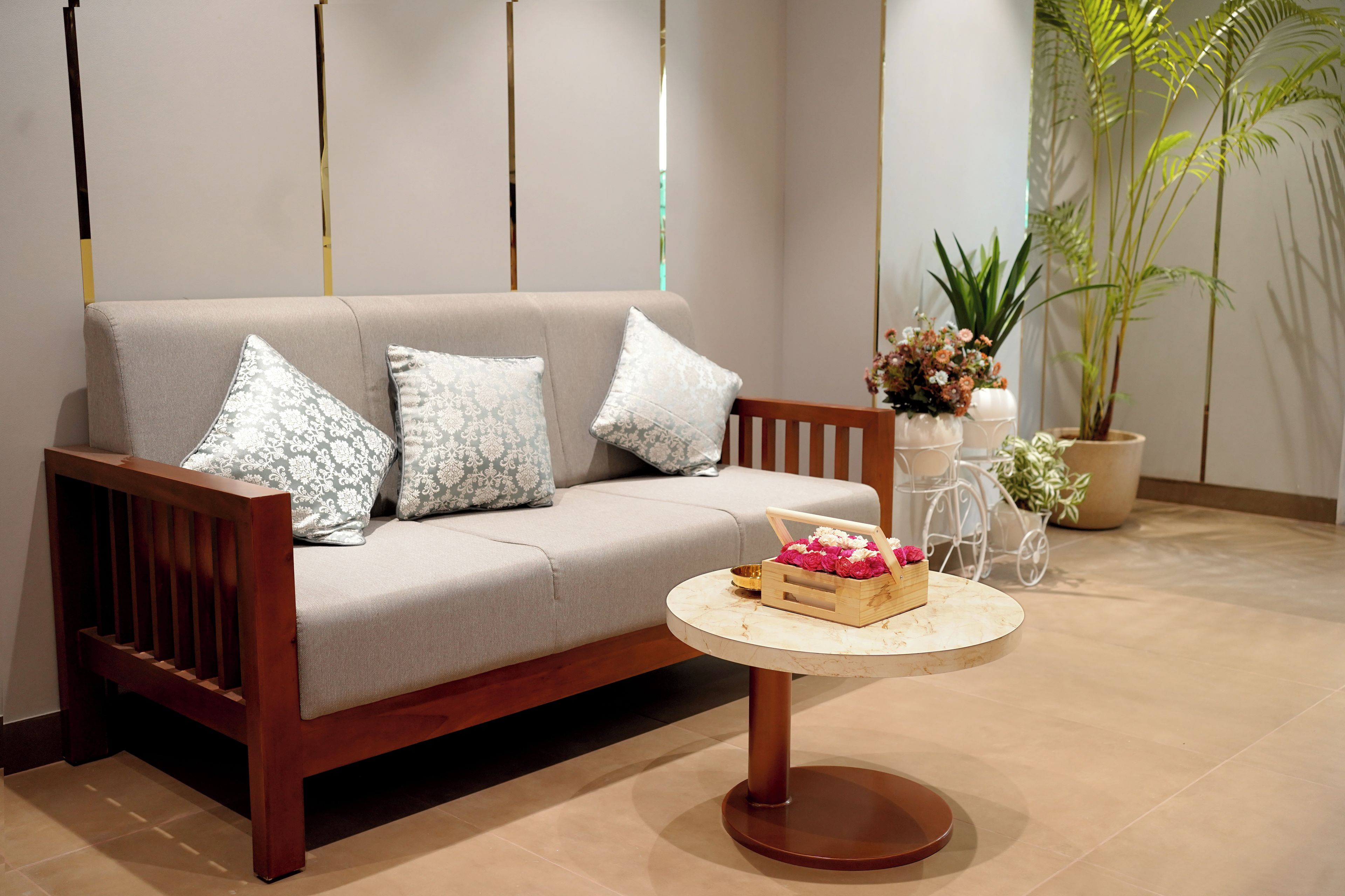 A sofa with patterned cushions, a wooden coffee table with a floral arrangement, and a potted plant in the background.