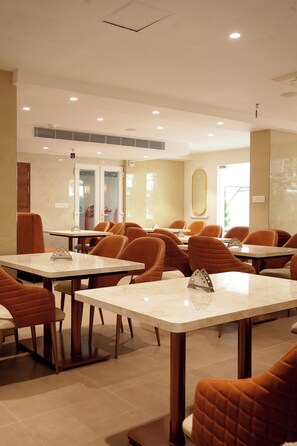 Ein Restaurantinnenraum mit mehreren Tischen und Stühlen, einer Decke mit eingelassener Beleuchtung und einer Tür mit satinierten Glasscheiben.