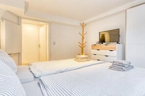 A hotel room with a bed, a TV, a wooden coat rack, and a wardrobe. - Holiday apartment with 2 bedrooms (Norderney)