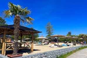 A beachside area with a palm tree, wooden structures, and beach chairs. - Holiday apartment with 2 bedrooms (Sierksdorf)