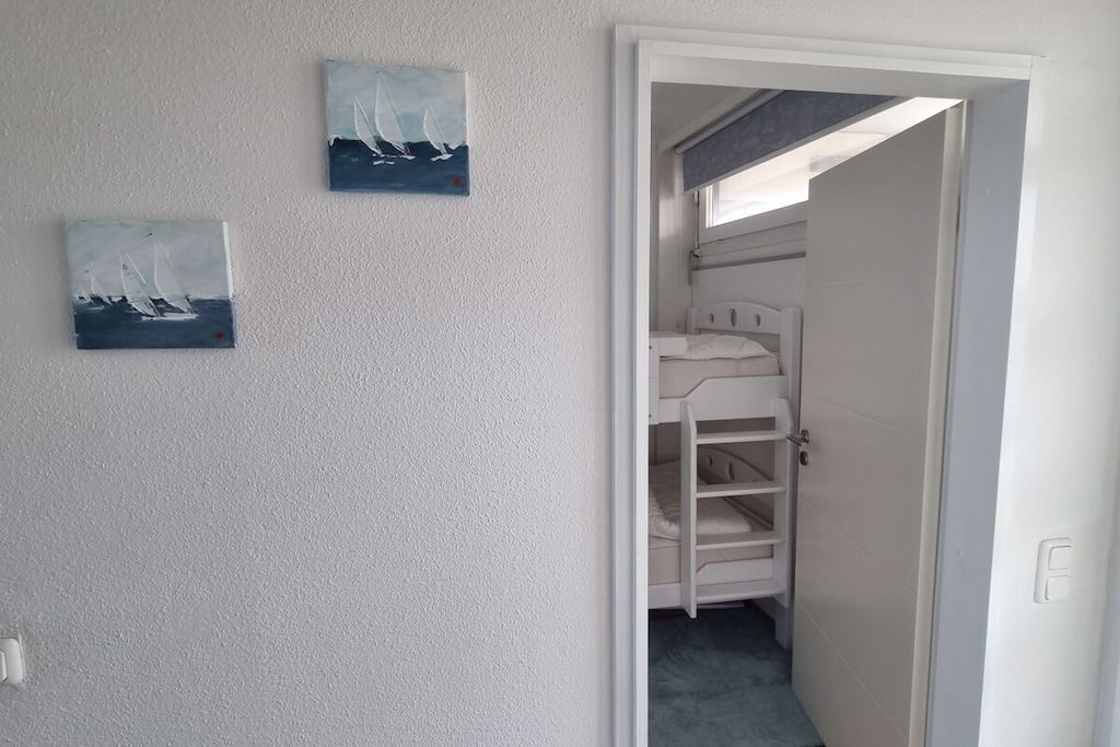 A room with a bunk bed, a door leading to another room, and two paintings on the wall.