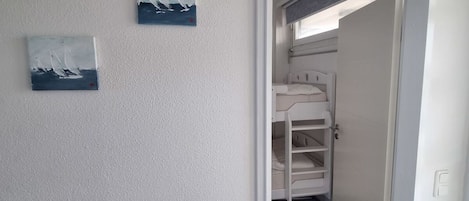 A room with a bunk bed, a door leading to another room, and two paintings on the wall.