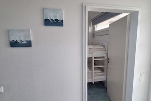 A room with a bunk bed, a door leading to another room, and two paintings on the wall. - Holiday apartment with 2 bedrooms (Sierksdorf)