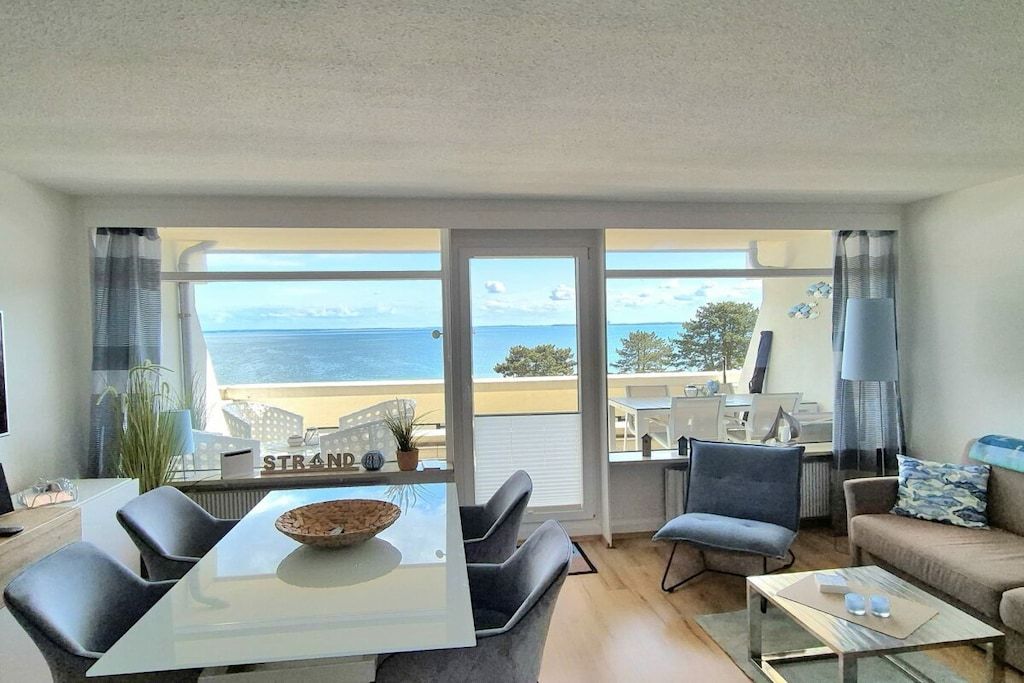 A living room with a dining table, chairs, a sofa, and a view of the sea.