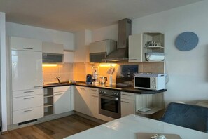 Een kleine keuken met witte kastjes, een magnetron, een oven en een koffiezetapparaat.