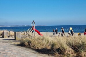 Een pad langs het strand met een rode glijbaan en een houten constructie, dat naar de zee leidt.